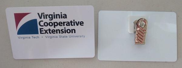 two plastic name badges side by side on a table. One is face up and shows the Virginia Cooperative Extension logo with a blank space. One is face down with a metal clip pointing up.