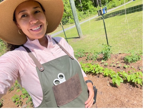 Woman with an apron poses in a vegetable garden.